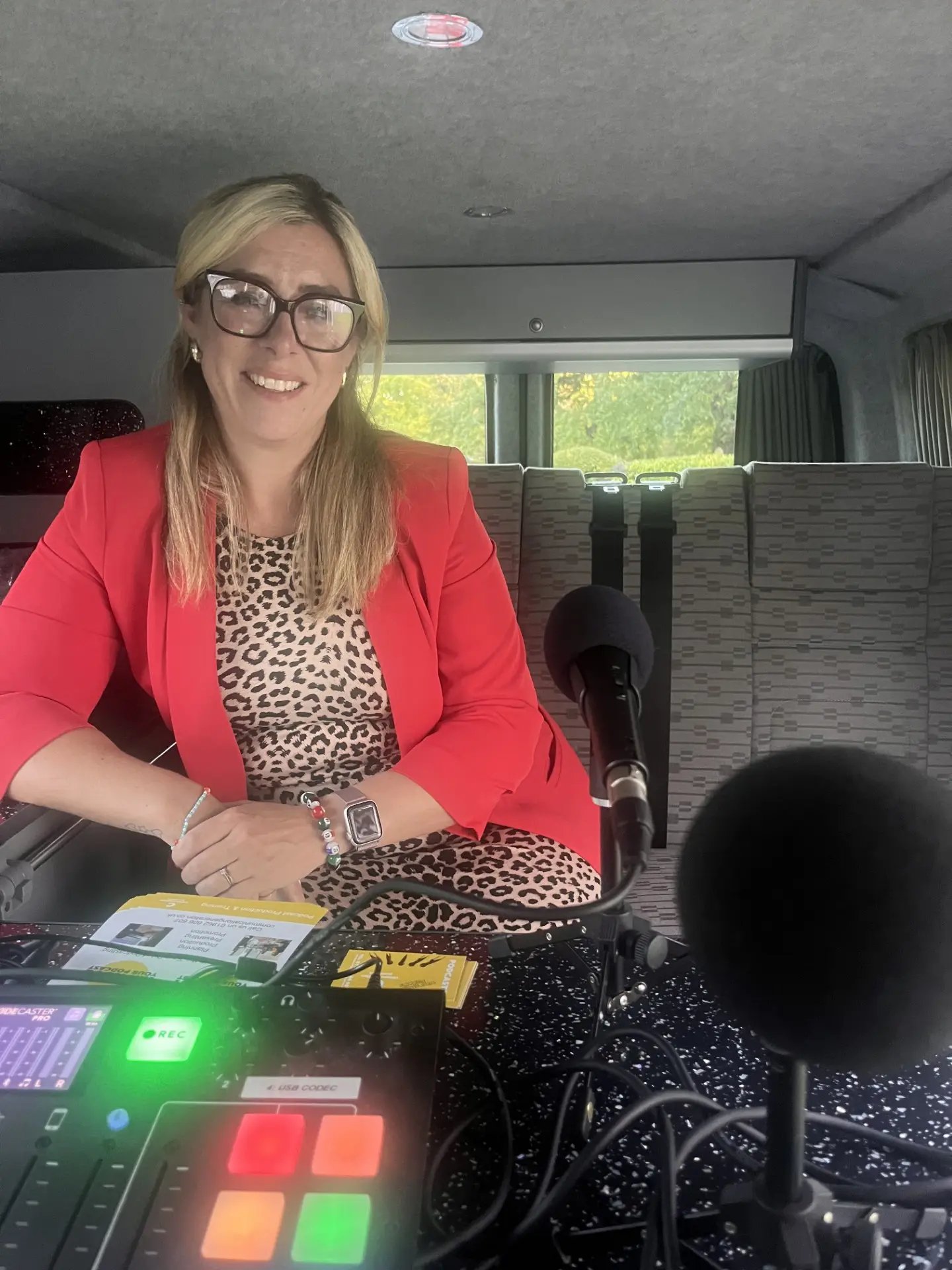 Lorna smiling behind the microphones, recording a podcast in a camper van